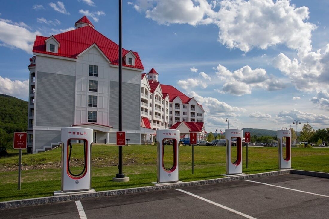 A building with a red roof and white walls, a Tesla charging station, and a parking lot.