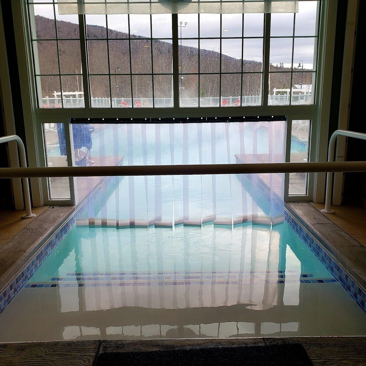 Une piscine intérieure avec des parois en verre transparent, un sol carrelé et une rambarde en métal.