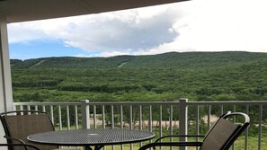 A balcony with a table and chairs overlooking a forested hillside.