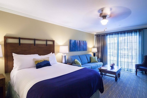 A hotel room with a large bed, a sofa, a coffee table, and a ceiling fan.
