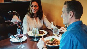 A dining table with plates of food, glasses, and a person pouring wine. - River Walk Resort at Loon studio, kitchenette, balcony, mount, river view, 5 fl (Lincoln)