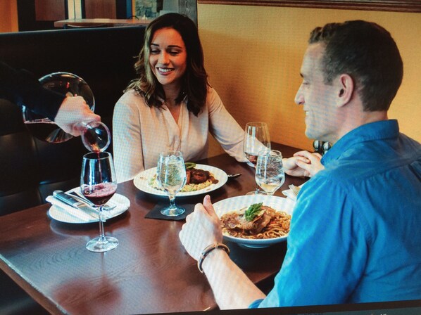 A dining table with plates of food, glasses, and a person pouring wine.