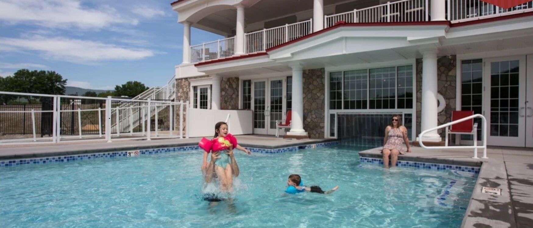 Uma área de piscina com deck coberto, parede de pedra e escadaria para uma varanda.