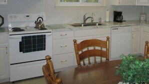 A compact kitchen with white cabinets, a stove, a sink, and a dining table with chairs. - Creek Side Home-Fly Fishing, Nature Walks (Boiling Springs)