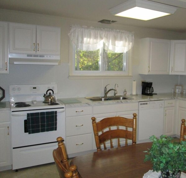 Cocina compacta con armarios blancos, estufa, lavamanos y una mesa de comedor con sillas.