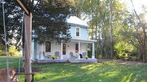 A two-story house with a porch, surrounded by trees and a swing set. - Creek Side Home-Fly Fishing, Nature Walks (Boiling Springs)