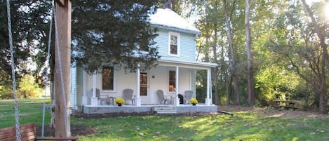 A two-story house with a porch, surrounded by trees and a swing set.