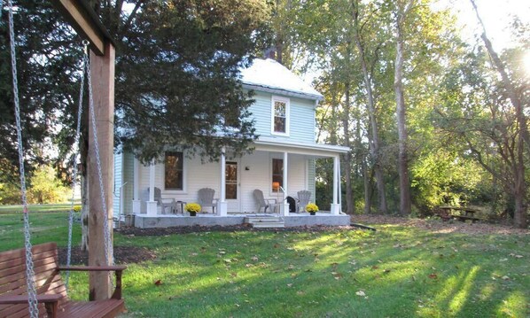 Une maison à deux étages avec un porche, entourée d’arbres et agrémentée d’une balançoire.