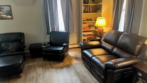 A living room with a black leather sofa, a black armchair, and a wooden floor. - Creek Side Home-Fly Fishing, Nature Walks (Boiling Springs)