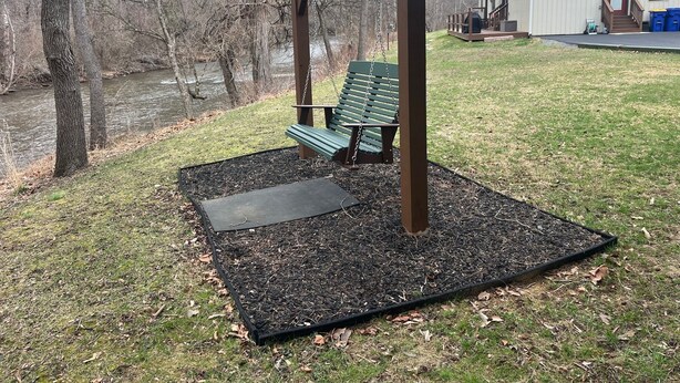 A wooden swing set with benches, a covered area, and a building in the background. - Creek Side Home-Fly Fishing, Nature Walks (Boiling Springs)