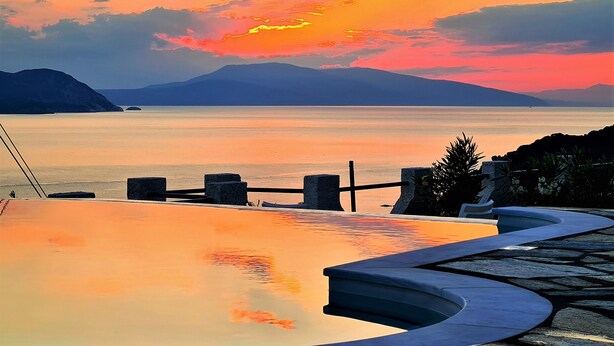 A pool with a view of the sea and mountains during sunset.