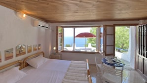 A bedroom with a bed, bedside table, and a window with a view of the sea.