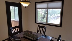 A dining area with a table, chairs, a bench, a hanging light fixture, and a window with blinds.