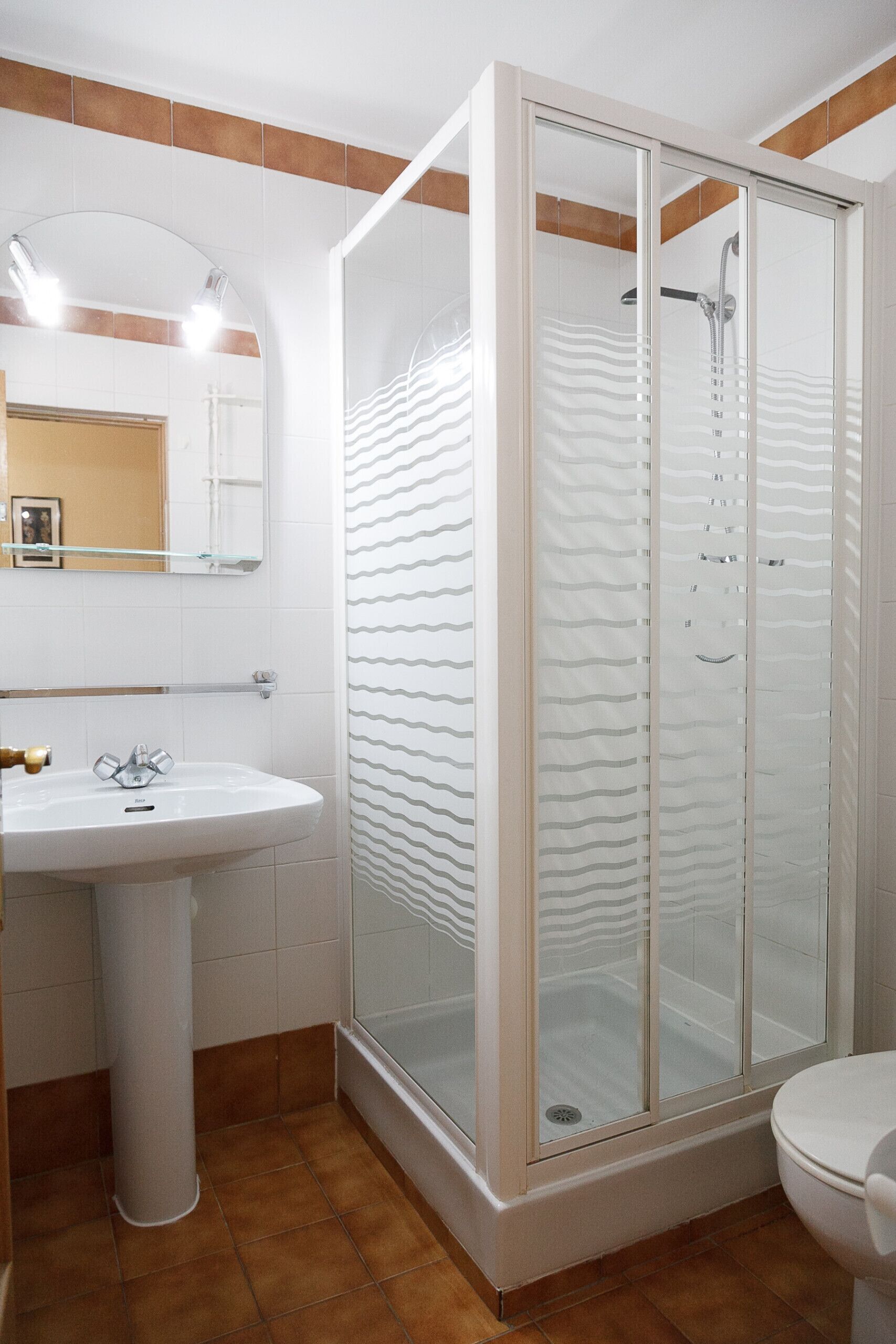 A bathroom with a glass-enclosed shower, a pedestal sink, and a toilet.