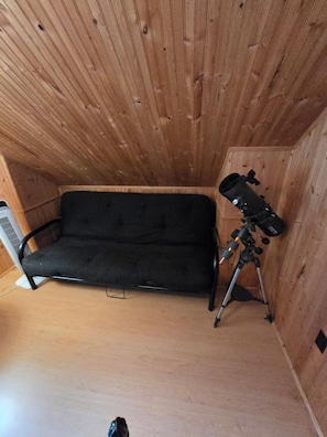A room with a wooden ceiling, a black sofa, and a telescope on a tripod. - Kawartha's Home/Cottage on Buckhorn Lake (Ennismore)