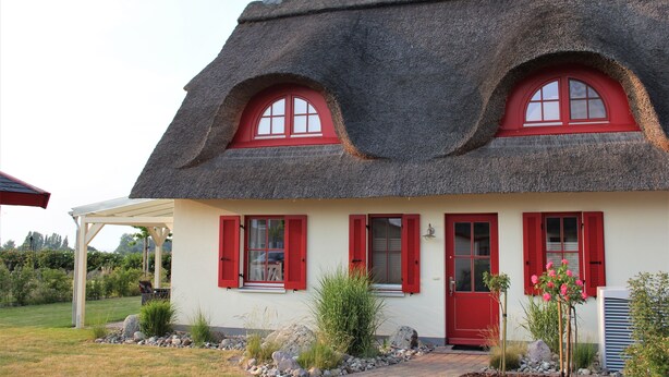 Ein Haus mit einem Strohdach, roten Fensterläden und einer weißen Fassade.
