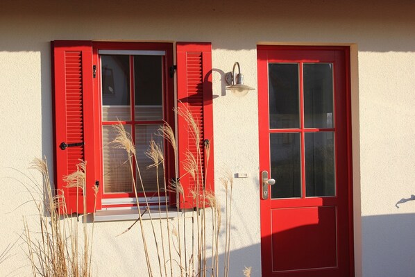 A building with a red door and window shutters, a light fixture above the door, and tall grasses in front. - Thatched cottage in 1. Row to the Baltic Sea - near the Hanseatic city of Wismar (Zierow)