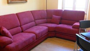 A red sectional sofa in a room with wooden flooring, a black chair, and a painting on the wall.