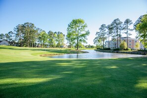 Un parcours de golf avec un étang, entouré d’arbres et de bâtiments.