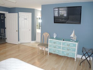 Une chambre à coucher avec un lit, une commode, une chaise, un téléviseur et une porte.