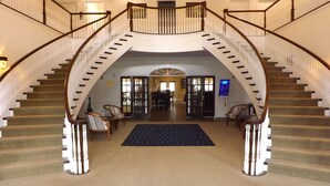 A grand staircase with a central landing, flanked by two sets of chairs and a carpeted area.