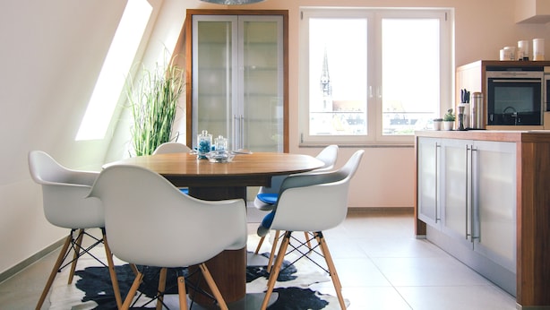 Un comedor con mesa de madera, sillas blancas y una lámpara colgante moderna.