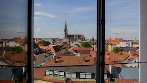 Vista de un paisaje urbano a través de una ventana, con una aguja de iglesia destacada, varios edificios y tejados.