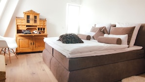 Un dormitorio con una cama, un aparador de madera y una silla blanca.