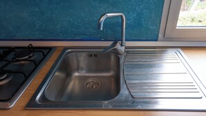 A stainless steel kitchen sink with a modern faucet, a gas stove, and a window with a view of greenery.