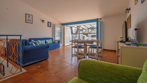 A living room with a blue sofa, a green armchair, and a dining area with a table and chairs.