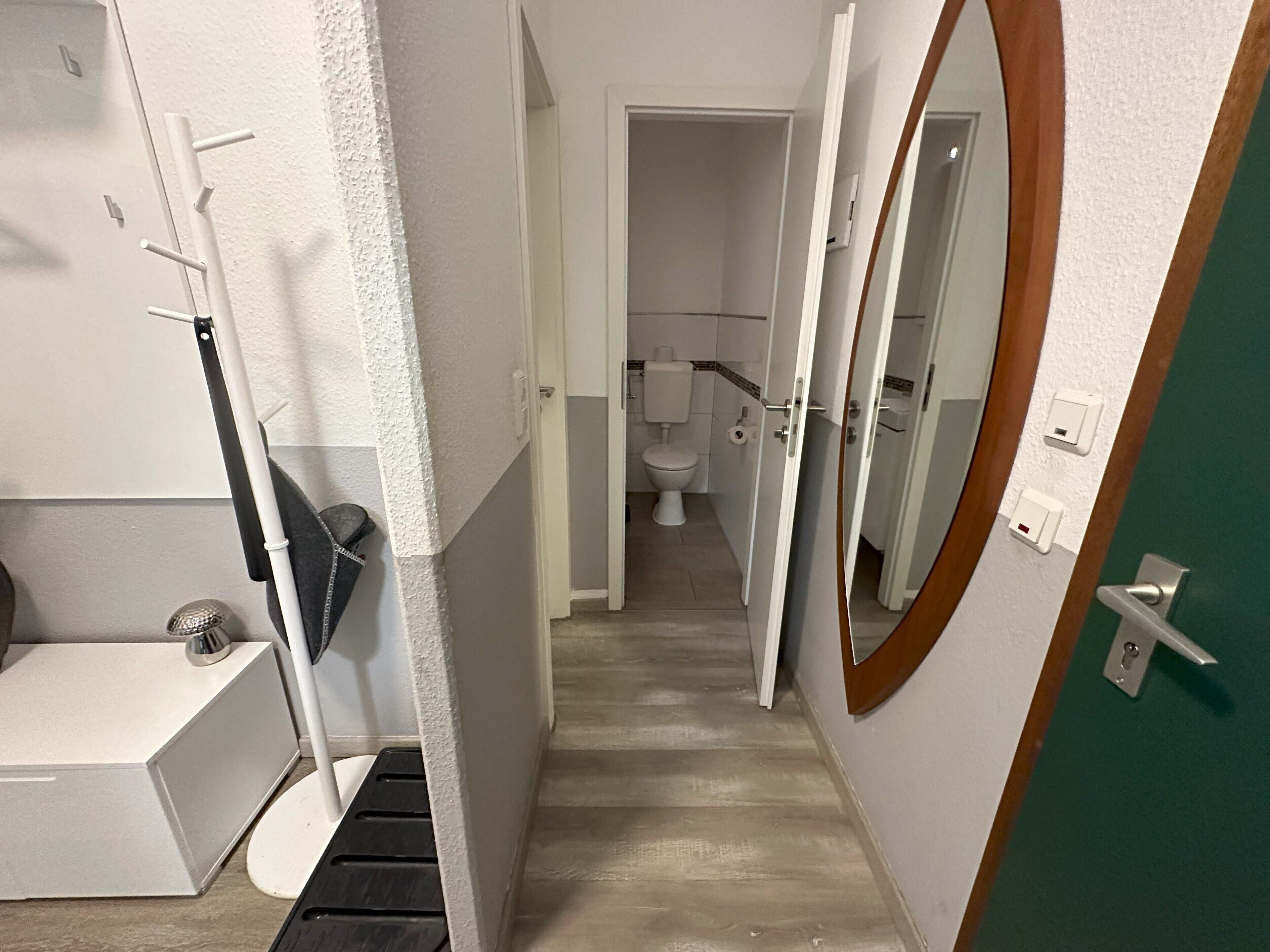 Ein schmaler Flur, der zu einem Badezimmer mit Toilette, Waschbecken und Spiegel führt.