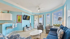 Un salon avec un canapé bleu, une table basse blanche et un téléviseur fixé au mur.