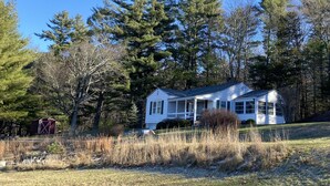 A single-story house with a porch, surrounded by trees and a grassy field. - Classic Cottage w/Beautiful Catskill View, on
5 peaceful acres. Weekly discount! (Stone Ridge)