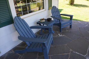 Two Adirondack chairs on a stone patio with a small table and a bowl between them.