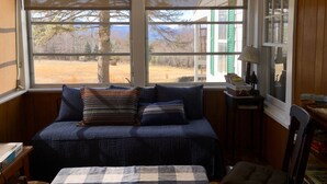 A bedroom with a large window, a bed with a blue quilt, a chair, and a lamp on a side table. - Classic Cottage w/Beautiful Catskill View, on
5 peaceful acres. Weekly discount! (Stone Ridge)