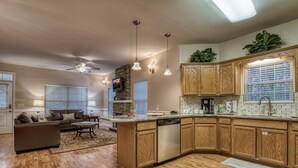 A spacious living room with a sofa and coffee table, a kitchen with wooden cabinets and a stone accent wall, and a ceiling fan. - Pigeon Forge Cottage w/ Hot Tub & City Lights, Near Dollywood Sleeps 7 (PIGEON FORGE, TN)
