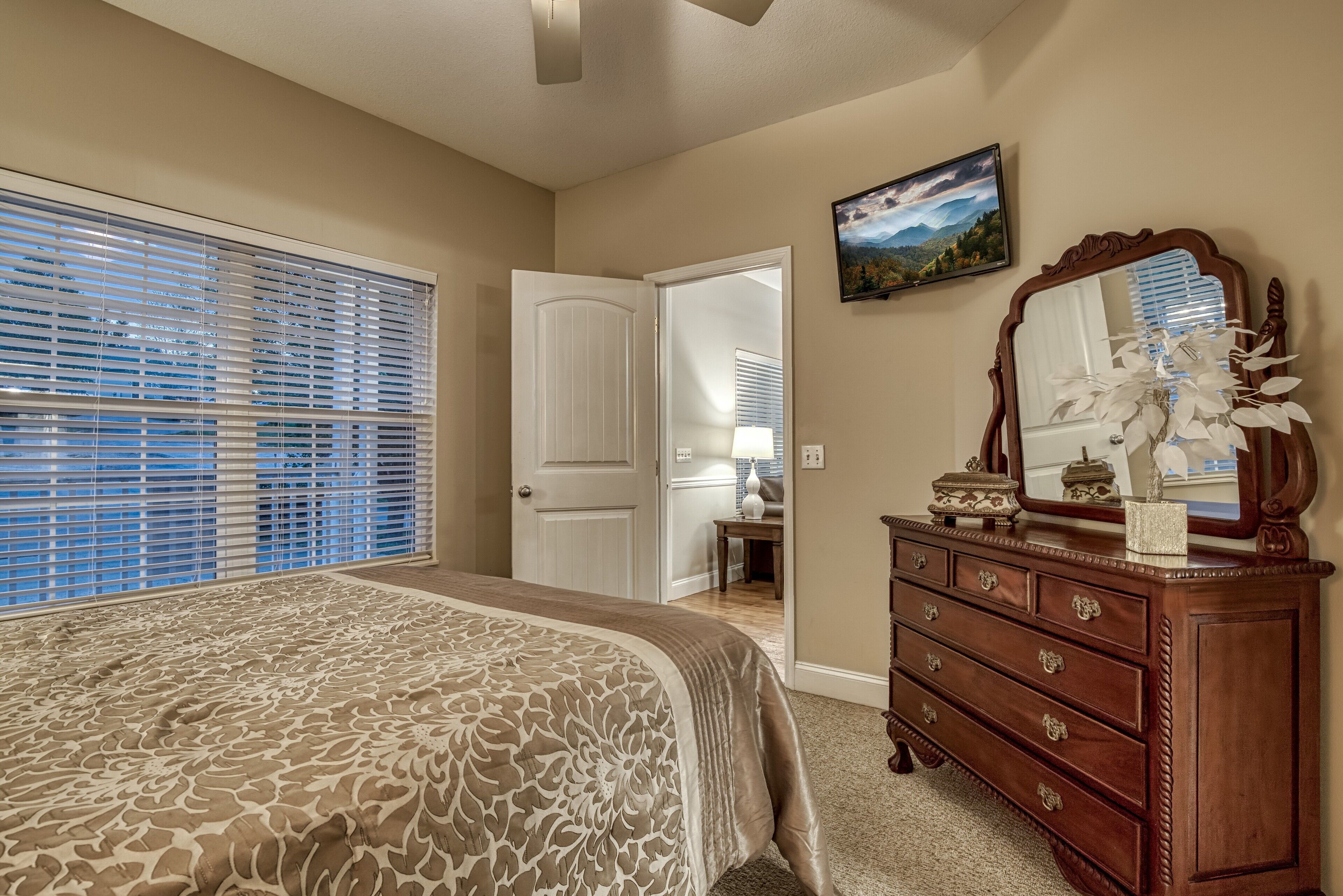 A bedroom with a large bed, a dresser, a mirror, and a door leading to another room.