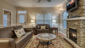 A living room with a stone fireplace, a ceiling fan, and a television mounted on the wall. - Pigeon Forge Cottage w/ Hot Tub & City Lights, Near Dollywood Sleeps 7 (PIGEON FORGE, TN)