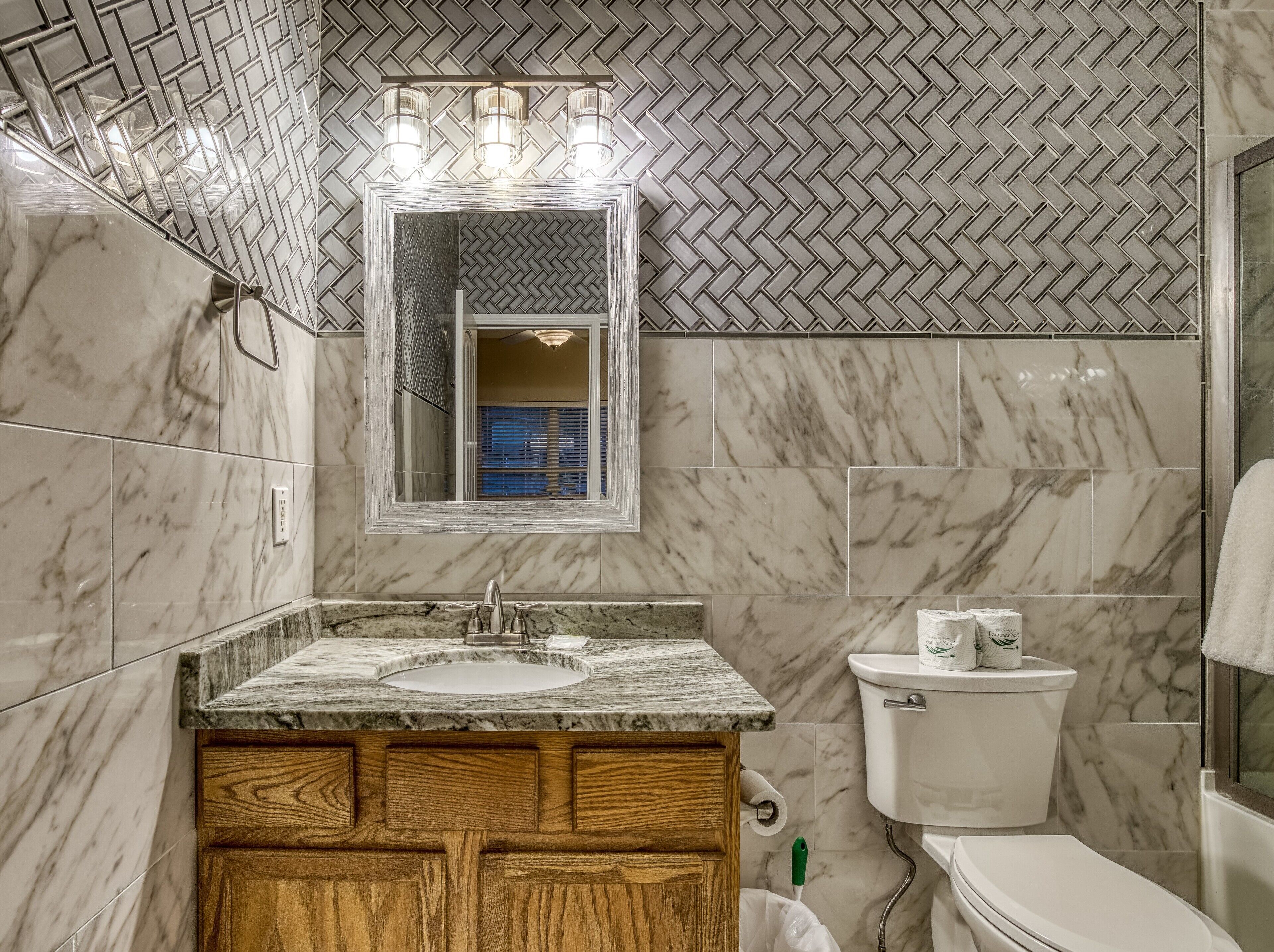 A bathroom with a marble sink, wooden vanity, a toilet, and a mirror with lights above.