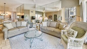 Ein geräumiges Wohnzimmer mit einem Glastisch, zwei Sofas, einem Korbstuhl und einem Deckenventilator.