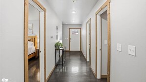 Un couloir avec un lit, une petite table sur laquelle est posée une plante, et une porte au fond.