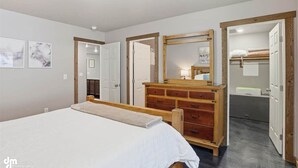 Une chambre à coucher avec un lit, une commode en bois et un miroir. Des portes donnent accès à d’autres pièces.