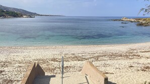 Une plage à l’eau claire, avec un rivage sablonneux et des affleurements rocheux.