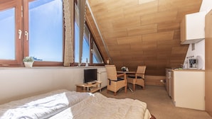 Quarto com cama, escrivaninha e cadeira. Há uma janela com persianas, um radiador e um pequeno vaso de planta.