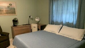 A bedroom with a bed, a desk, a chair, a fan, a lamp, and a painting on the wall. - Clean And Comfortable  (Sebring)