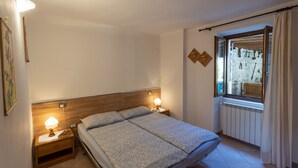 A bedroom with a bed, two bedside tables with lamps, a window with curtains, and a radiator. - CASA RITA - AP. N. 4 LAKE GARDA TREMOSINE (Vesio)
