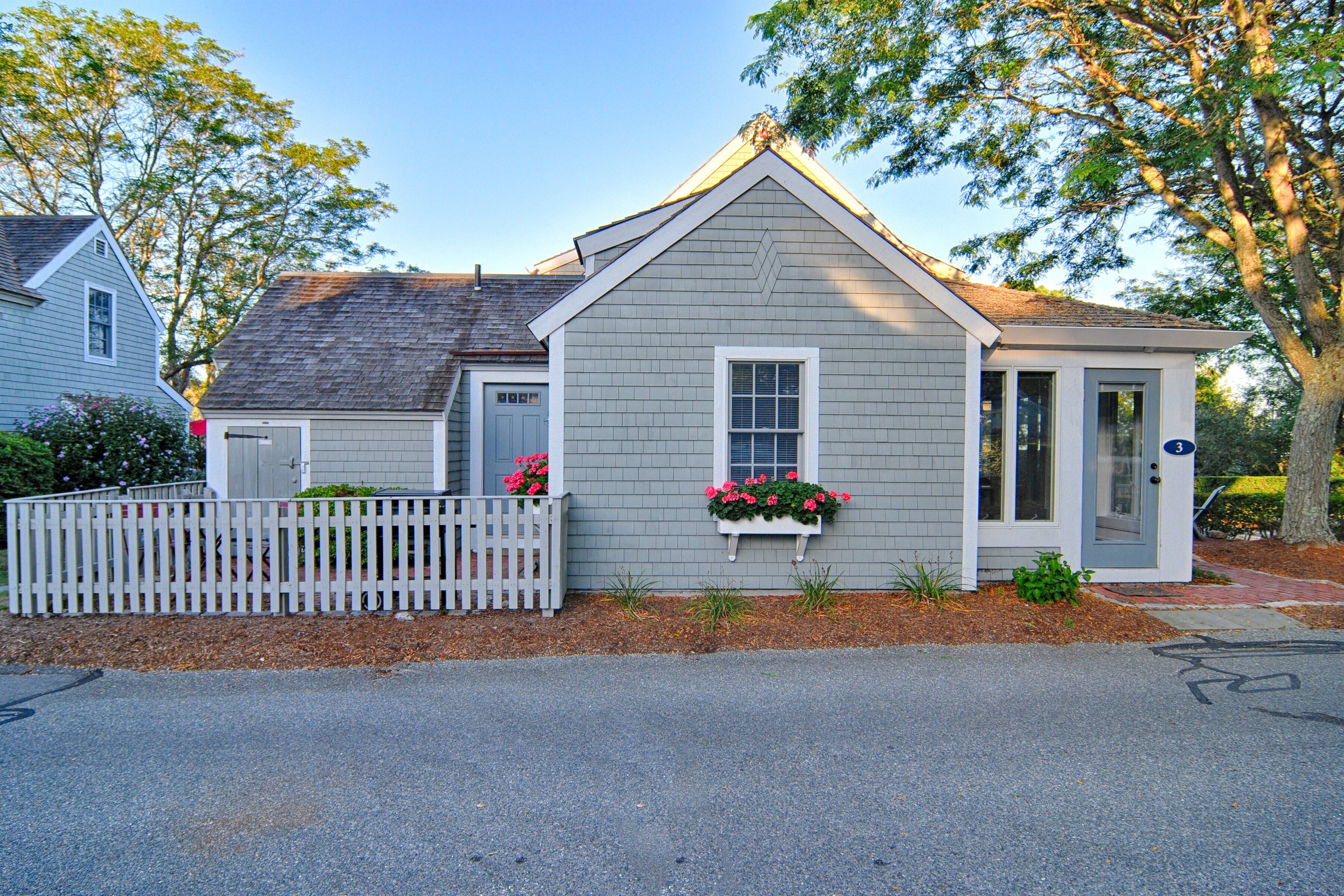 A single-story house with a gray exterior, a white picket fence, and flower boxes on the front porch.