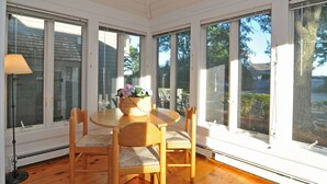 A sunlit room with a round table and four chairs, large windows, and a basket of flowers on the table. - Private condo in Maushop. Steps to beach, ocean, Popponesset Inn and Marketplace (Mashpee)