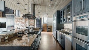 Une cuisine moderne avec un pare-feu en pierre, des appareils en acier inoxydable et un plafond en bois.