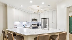 A spacious kitchen with white cabinetry, a large island with bar stools, stainless steel appliances, and a modern chandelier. - Picturesque Villa w/ Screened Porch & Amenities (Hilton Head Island)